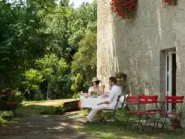 Mesa con sillas rojas para comer al aire libre junto a un muro de piedra en A Quinta da Auga