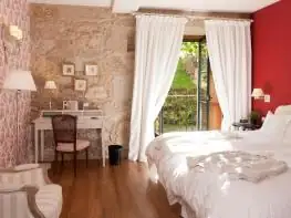 Habitación con paredes de piedra, escritorio y ventanal con cortinas blancas en A Quinta da Auga