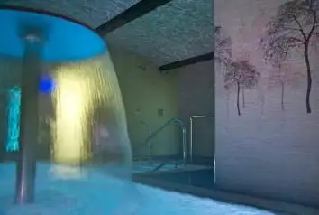 Cascada de agua iluminada sobre la piscina termal interior del Balneario Acuña
