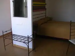 Habitación con cama, portamaletas de forja y espejo en el Balneario Acuña