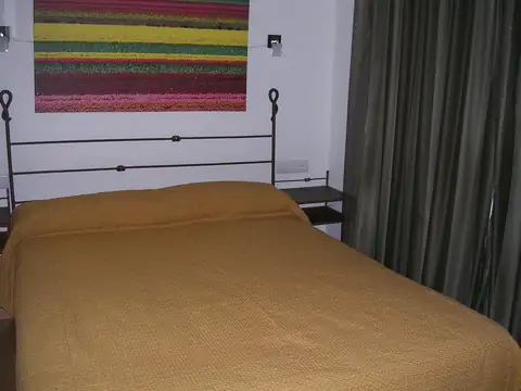 Cama de matrimonio con cabecero de forja y colcha dorada en el Balneario Acuña
