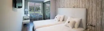 Habitación twin con camas blancas y ventana al jardín en el Arnoia Caldaria Hotel Balneario