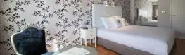 Habitación con papel pintado floral, sillón y cama de matrimonio en el Balneario Arnoia