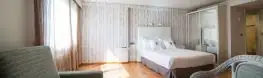 Amplia habitación con suelo de madera, armario de espejo y sillones del Balneario Arnoia
