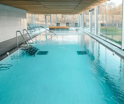 Piscina interior alargada con escalerillas y paredes acristaladas en el Balneario Caldas de Partovia