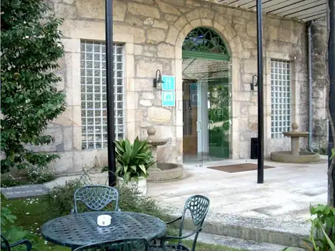 Terraza ajardinada con mesa de forja junto a la entrada del Hotel Balneario de Caldelas de Tui