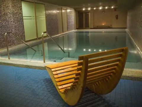 Piscina interior iluminada con tumbona ergonómica de madera en el Hotel Balneario de Compostela