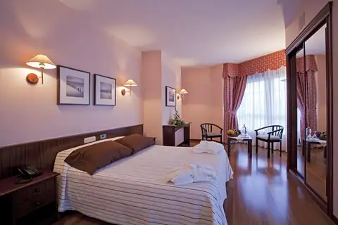 Habitación doble con suelo de madera y zona de estar junto a la ventana del Balneario de Carballo