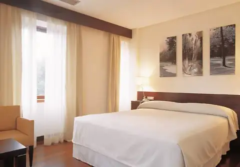 Habitación con cama de matrimonio, butaca y cuadros en el Iberik Gran Balneario de Guitiriz