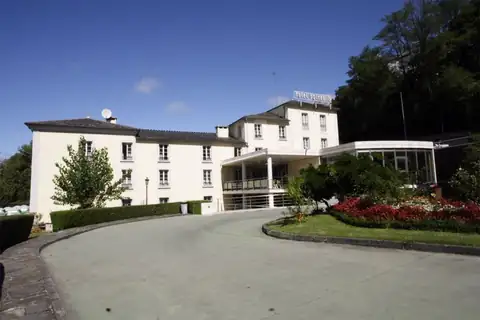Fachada blanca y jardín con flores a la entrada del Hotel Balneario de Lugo – Termas Romanas