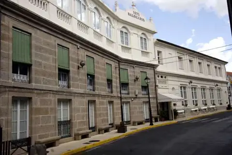 Fachada de piedra y galería blanca del edificio del Balneario de Baños de Molgas junto a la calle