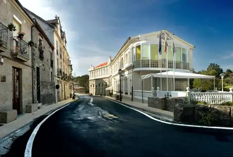 Vista exterior del Balneario de Baños de Molgas con banderas y terraza en la calle del pueblo