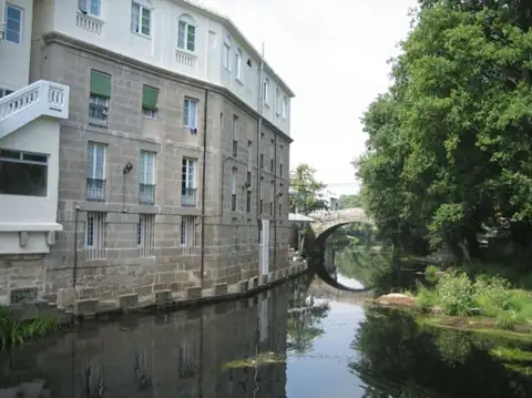 Edificio de piedra del Balneario de Baños de Molgas junto al río y un puente de piedra