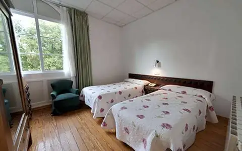 Habitación con dos camas, butaca verde y suelo de madera en el Balneario de Baños de Molgas