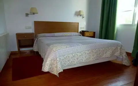 Habitación doble con cama de matrimonio y mesillas de madera en el Balneario de Molgas