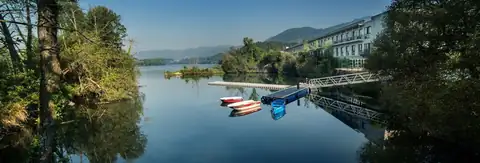 Embarcadero con barcas en el río y el hotel entre la vegetación de Laias Caldaria