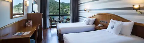 Habitación con dos camas, escritorio y ventanal al río en el Laias Caldaria Hotel Balneario