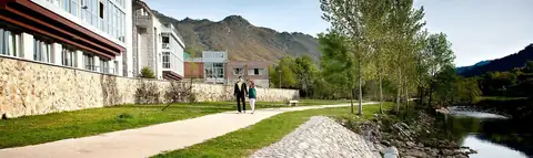 Paseo junto al río y la fachada del hotel con montañas al fondo en Lobios Caldaria