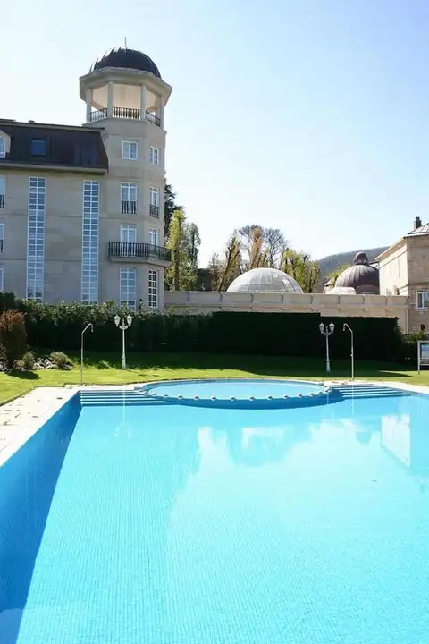 Piscina exterior con césped junto al edificio con torre del Balneario de Mondariz