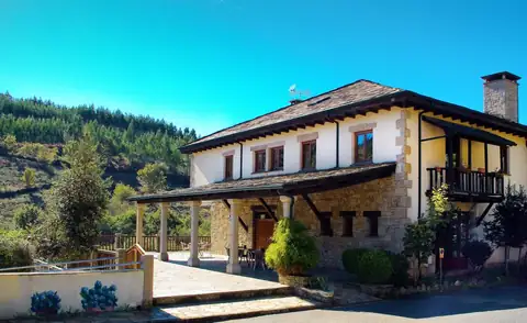 Edificio de piedra y madera con balcón del Hotel Balneario Río Pambre rodeado de monte