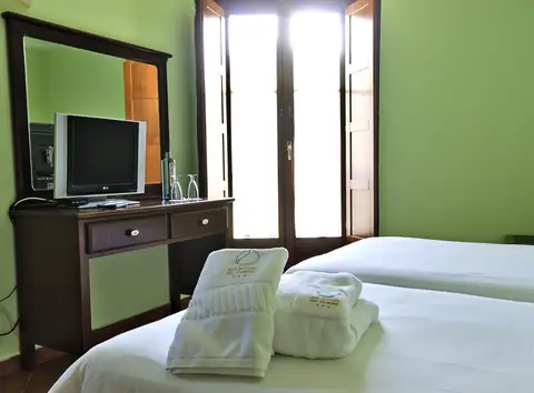 Toallas sobre la cama, tocador con televisión y ventana en una habitación del Balneario Río Pambre