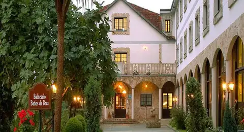 Patio de entrada con farolas y fachada de piedra al anochecer del Hotel Balneario Baños da Brea