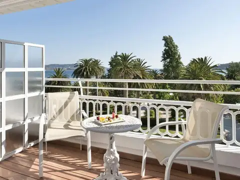 Balcón de habitación con mesa y sillones blancos frente a las palmeras y la ría en el Gran Hotel La Toja