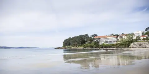 Playa de arena con el Gran Talaso Hotel Sanxenxo entre los árboles al fondo