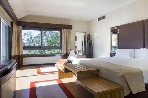 Amplia habitación con cama de matrimonio, banco de madera y ventanal en el Gran Talaso Hotel Sanxenxo