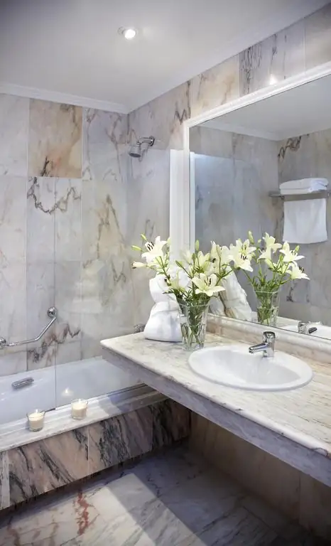 Baño de mármol con bañera, lavabo y flores en una habitación del Hotel Carlos I Silgar