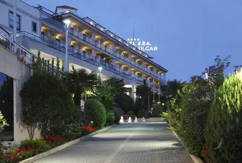 Fachada del Hotel Carlos I Silgar al anochecer con camino de acceso ajardinado