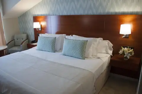 Habitación doble con cabecero de madera y cojines azules en el Hotel Carlos I Silgar