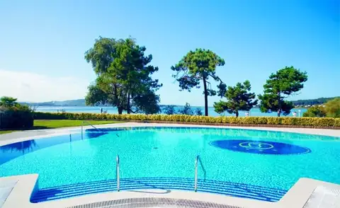 Piscina exterior rodeada de césped y pinos con la ría al fondo en el Eurostars Isla de la Toja