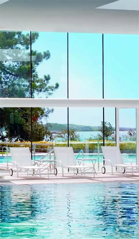 Piscina interior con tumbonas y grandes ventanales abiertos a la ría en el Eurostars Isla de la Toja
