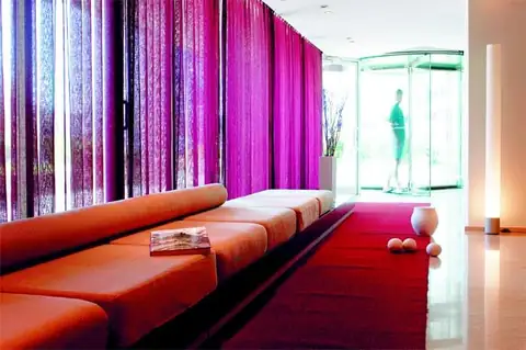 Vestíbulo con sofá rojo alargado y cortinas fucsia en el Eurostars Isla de la Toja