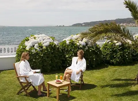 Dos huéspedes en albornoz en el jardín con hortensias frente a la ría del Eurostars Louxo Talaso