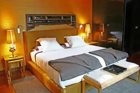 Habitación con cama de matrimonio, banqueta y luz cálida en el Gran Hotel Nagari de Vigo