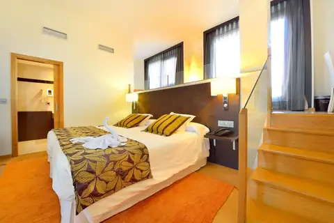 Habitación doble con escalera de madera y cama con colcha estampada en el Hotel Norat Marina & Spa