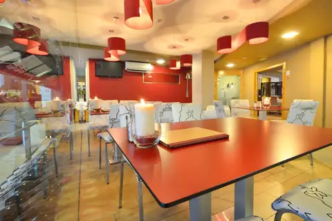 Cafetería con mesas rojas y lámparas colgantes en el Hotel Norat Marina & Spa
