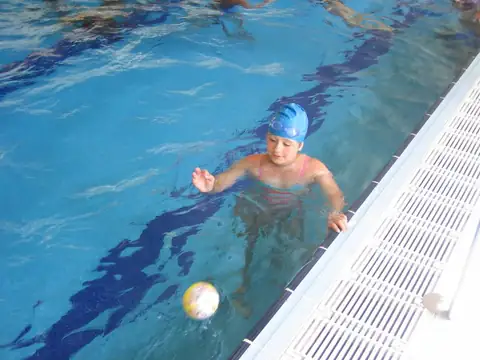 Niño con gorro nadando con una pelota en la piscina cubierta de los Apartamentos Manzaneda