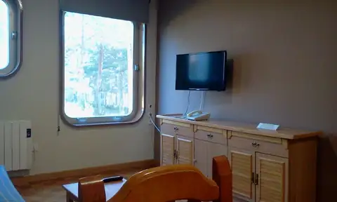 Salón con televisión, aparador de madera y ventana redondeada en los Apartamentos Manzaneda