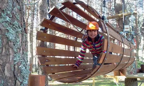 Niña con casco atravesando un túnel de madera en el parque de aventura de Manzaneda