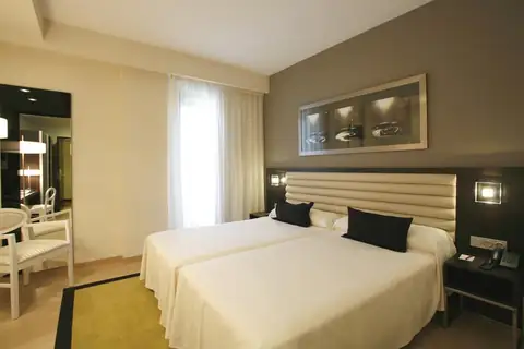 Habitación con dos camas, cabecero acolchado y butaca blanca en el Hotel Bienestar Moaña