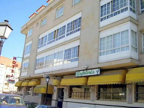 Fachada del edificio con galerías blancas y cafetería con toldos amarillos del Hotel Spa Norat O Grove