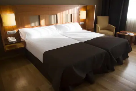 Habitación con dos camas juntas y sillón de lectura en el Exe Vía Argentum