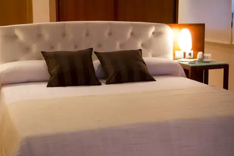 Cama de matrimonio con cabecero capitoné y cojines oscuros en el Exe Vía Argentum