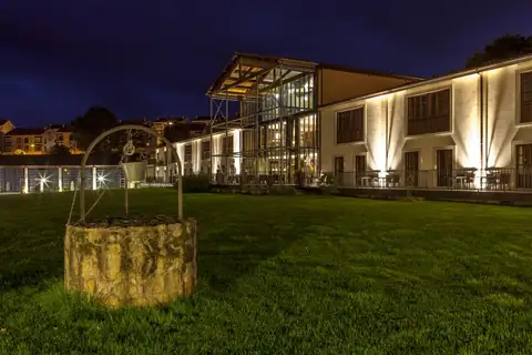 Jardín con pozo de piedra y edificio iluminado de noche en el Eurostars Vila de Allariz