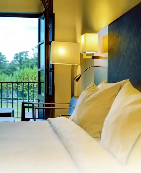 Detalle de cama con cojines y ventana al jardín en una habitación del Eurostars Vila de Allariz