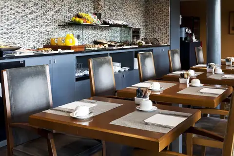Comedor del desayuno con mesas de madera y bufé al fondo en el Eurostars Vila de Allariz