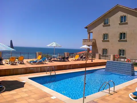Piscina exterior con tumbonas y vistas al mar junto al edificio del Hotel Talaso Atlántico